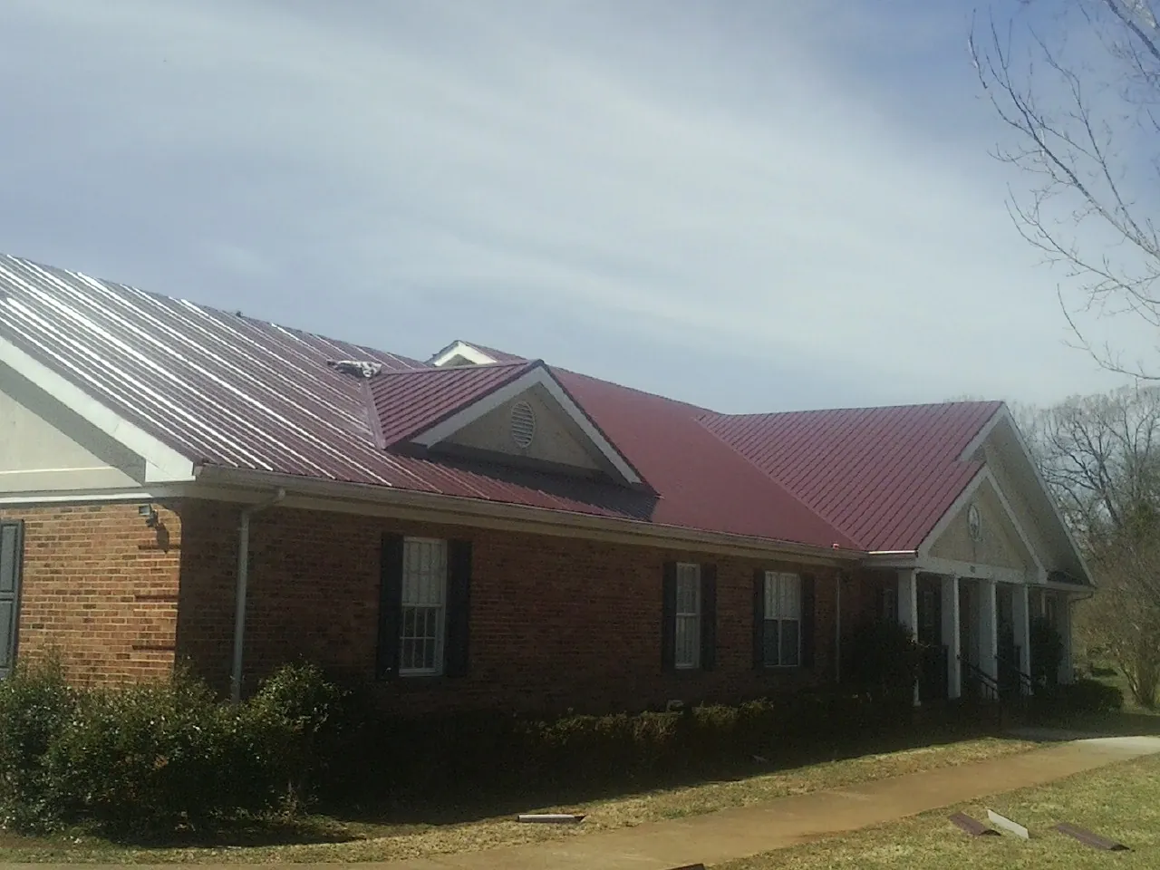 Red metal roof with gabled entries on a long brick building, from a Hail Damage Roof Repair job in Kensington